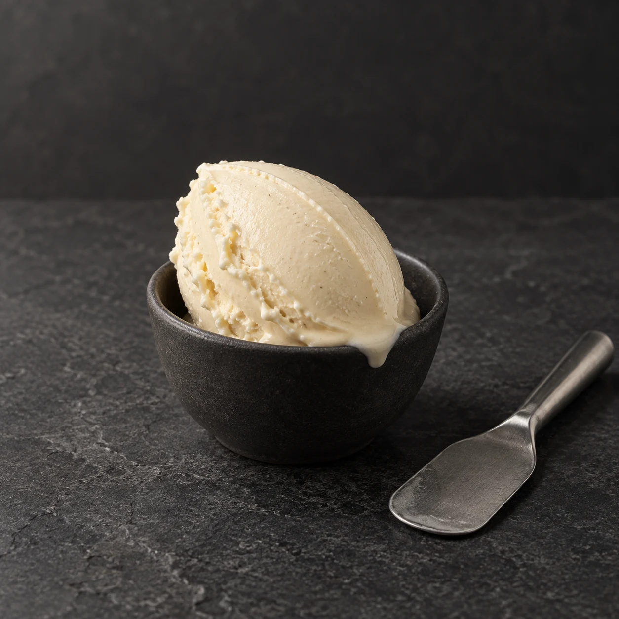 Una quenelle di gelato color avorio in una coppetta scura su pietra