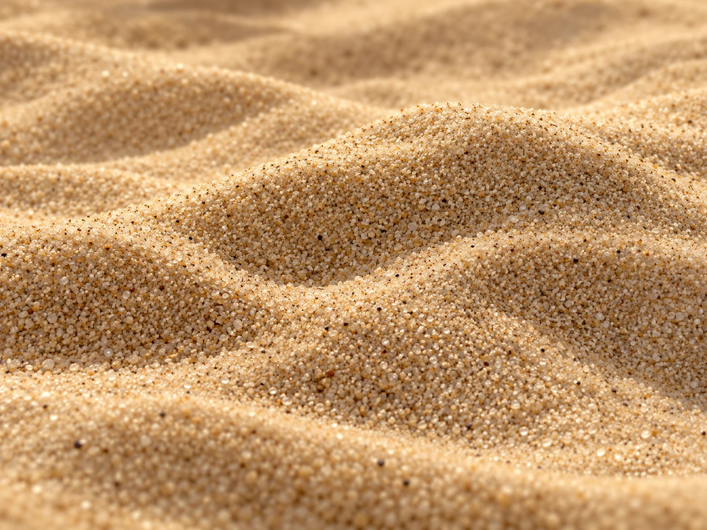 Piccole dune di sabbia beige chiara con granelli illuminati da una luce morbida.
